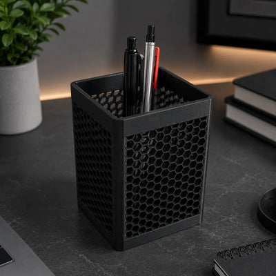 3D printed honeycomb hexagon mesh square pen holder in matte black holding pens and markers on a dark desk
